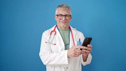 Wall Mural - Middle age grey-haired man doctor smiling confident using smartphone over isolated blue background