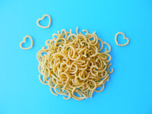 Uncooked curly pasta with heart shaped noodles on blue background top view        