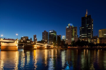 Stunning  of Frankfurt's skyline at night featuring a bridge, skyscrapers, traffic with light trails, and dazzling city illumination reflecting in the river.