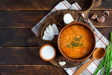 Wall Mural - Cabbage soup in bowl with green onion, bread and salo on wooden background. Top view