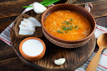 Wall Mural - Cabbage soup in bowl with green onion, bread and salo on wooden background