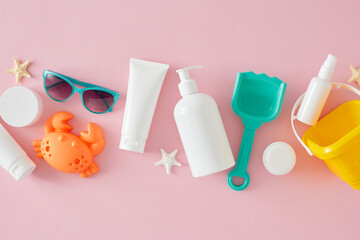 Concept for children's summer skin care. Top view flat lay of sunscreen bottles, starfish, sand molds for beach  and sunglasses on light pink background