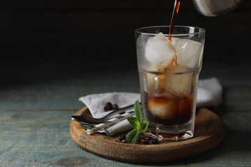 Poster - Pouring coffee into glass with ice cubes, mint and beans on light blue wooden table, space for text