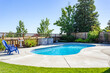 A pool in a residential backyard with blue chairs, green trees and a blue sky. Great for virtual staging