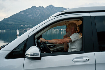 Wall Mural - Happy older man driving rv camper van on vacation trip. Smiling mature active traveler sitting in campervan trailer enjoying camping tourism in nature park with lake and mountains travel journey.