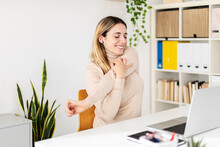 Young Adult Woman Sitting On Home Office Table Stretching Arms While Working On Laptop Computer. Freelancer Female Worker Taking Break From Work. Health Concept