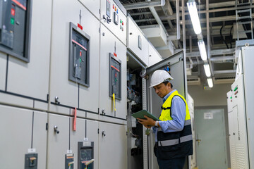 Wall Mural - Professional Asian male engineer in safety uniform working at factory server electric control panel room. Industrial technician worker maintenance checking power system at manufacturing plant room.