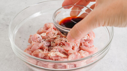 Wall Mural - Adding soy sauce to chopped chicken fillet . Glass bowl with the chopped marinated chicken meat close-up