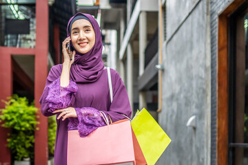 Modern lifestyle of arab muslim young woman in veil hijab holding shopping bags walking on the city street. while talking on mobile phone