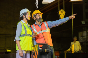 Young indian male and female engineers or construction workers wearing safety helmet and vest working together at Industrial factory.