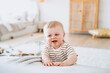© Iona - Little boy stands at living room leans on couch learning to walk smiles. Cheerful caucasian newborn baby  plays at home. Childhood, healthy children. Swedish toddler entertaining at bedroom.