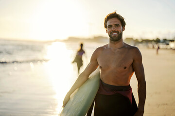 Wall Mural - Portrait of a fit man with surfboard on a beach smiling at the camera.