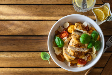 Poster - Dinner plate with potato gnocchi, grilled chicken breast, parmesan cheese and tomatoes on wooden table. Italian food concept