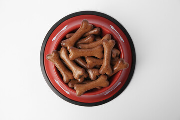 Wall Mural - Red bowl with bone shaped dog cookies on white background, top view