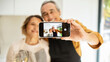 Selfie at romantic dinner. Happy senior couple taking selfie on smartphone in kitchen interior, selective focus