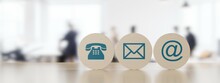 Wooden Round Telephone, Envelope Letter And E-mail Symbols In A Row On Wooden Table With A Blurred Office In The Background, Contact Us Symbols Or Banner
