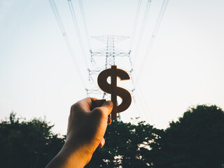 Businessman's hand holding a symbol Dollar with electric pole background, concept of electricity bills, electricity generation, public utility bills.
