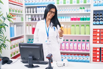 Wall Mural - Middle age hispanic woman pharmacist using computer holding pills bottle at pharmacy