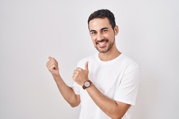 Poster - Handsome hispanic man standing over white background pointing to the back behind with hand and thumbs up, smiling confident