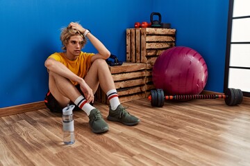 Poster - Young blond man tired sitting on floor at sport center