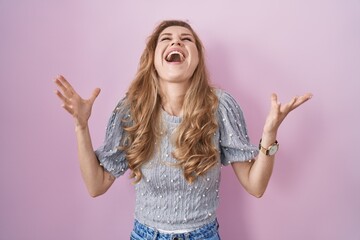 Sticker - Beautiful blonde woman standing over pink background celebrating mad and crazy for success with arms raised and closed eyes screaming excited. winner concept