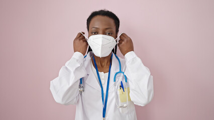 African american woman doctor wearing medical mask over isolated pink background