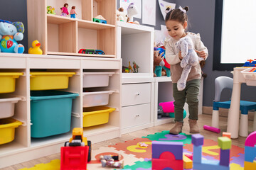 Wall Mural - Adorable hispanic girl smiling confident holding doll at kindergarten