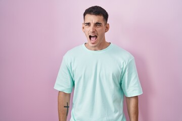 Poster - Handsome hispanic man standing over pink background angry and mad screaming frustrated and furious, shouting with anger. rage and aggressive concept.