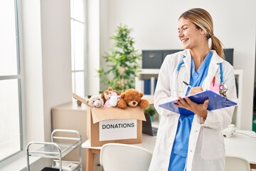 Wall Mural - Young hispanic woman wearing doctor uniform writing report for donations toys at clinic