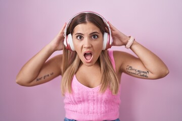 Canvas Print - Young blonde woman listening to music using headphones crazy and scared with hands on head, afraid and surprised of shock with open mouth