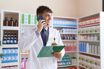 Poster - Young hispanic man pharmacist talking on smartphone reading document at pharmacy