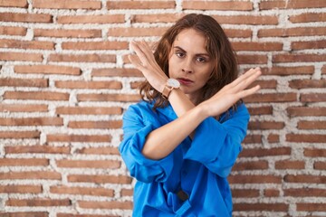 Poster - Beautiful brunette woman standing over bricks wall rejection expression crossing arms doing negative sign, angry face