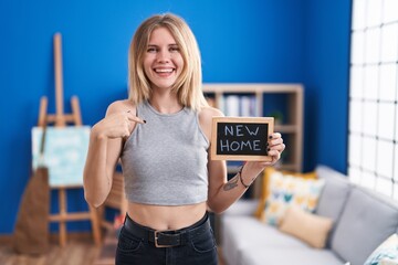 Sticker - Blonde caucasian woman holding blackboard with new home text pointing finger to one self smiling happy and proud