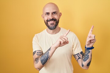 Sticker - Hispanic man with tattoos standing over yellow background smiling and looking at the camera pointing with two hands and fingers to the side.