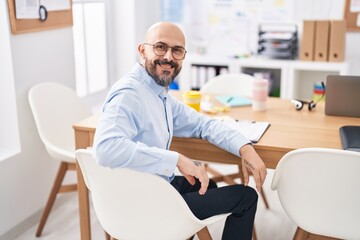 Canvas Print - Young bald man business worker smiling confident sitting on table at office