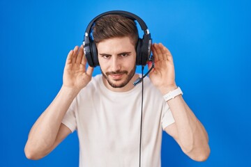 Poster - Hispanic man with beard listening to music wearing headphones trying to hear both hands on ear gesture, curious for gossip. hearing problem, deaf