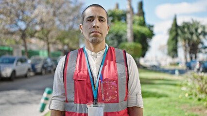 Sticker - Young hispanic man volunteer wearing vest looking serious at park