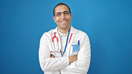 Poster - Young hispanic man doctor smiling confident standing with arms crossed gesture over isolated blue background