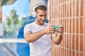 Wall Mural - Young caucasian man smiling confident playing video game at street