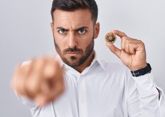 Canvas Print - Handsome hispanic man holding cardano cryptocurrency coin pointing with finger to the camera and to you, confident gesture looking serious