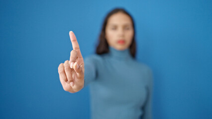 young beautiful hispanic woman saying no with finger over isolated blue background