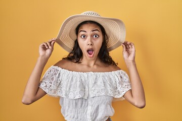 Sticker - Young brazilian woman wearing summer hat over yellow background afraid and shocked with surprise and amazed expression, fear and excited face.