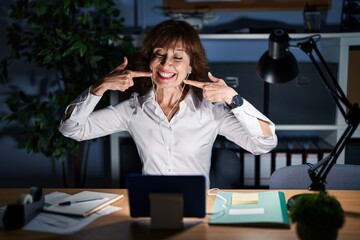 Wall Mural - Middle age woman working at the office at night smiling cheerful showing and pointing with fingers teeth and mouth. dental health concept.