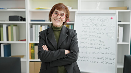 Sticker - Mature hispanic woman teacher standing by white board with crossed arms at library university