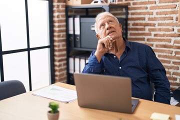 Poster - Senior man with grey hair working using computer laptop at the office serious face thinking about question with hand on chin, thoughtful about confusing idea