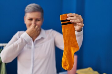 Sticker - Middle age woman smiling confident smelling dirty sock at laundry room