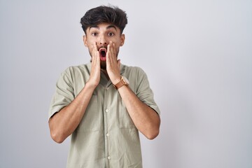 Poster - Arab man with beard standing over white background afraid and shocked, surprise and amazed expression with hands on face