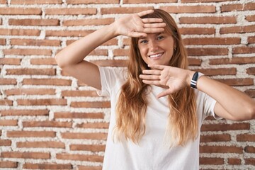 Sticker - Young caucasian woman standing over bricks wall smiling cheerful playing peek a boo with hands showing face. surprised and exited