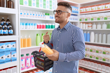 Poster - Young hispanic man customer smiling confident holding shampoo bottle and market basket at pharmacy