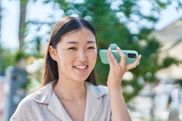 Wall Mural - Chinese woman smiling confident listening audio message by the smartphone at park